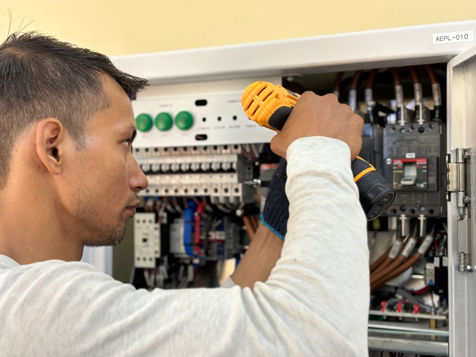 Electrician using a power tool inside an open switchboard