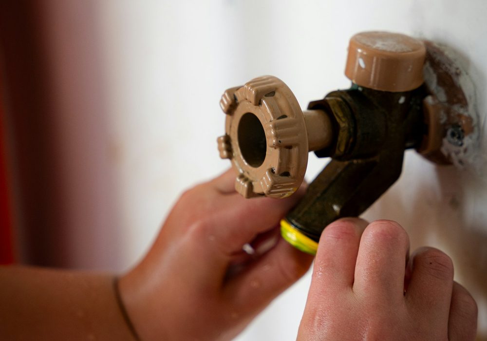 Close-up of hands using a wrench on a brass valve and white plumbing