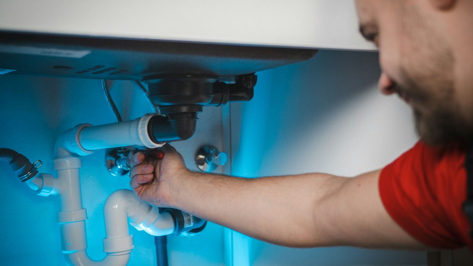 Plumber working under a sink on supply and drain lines