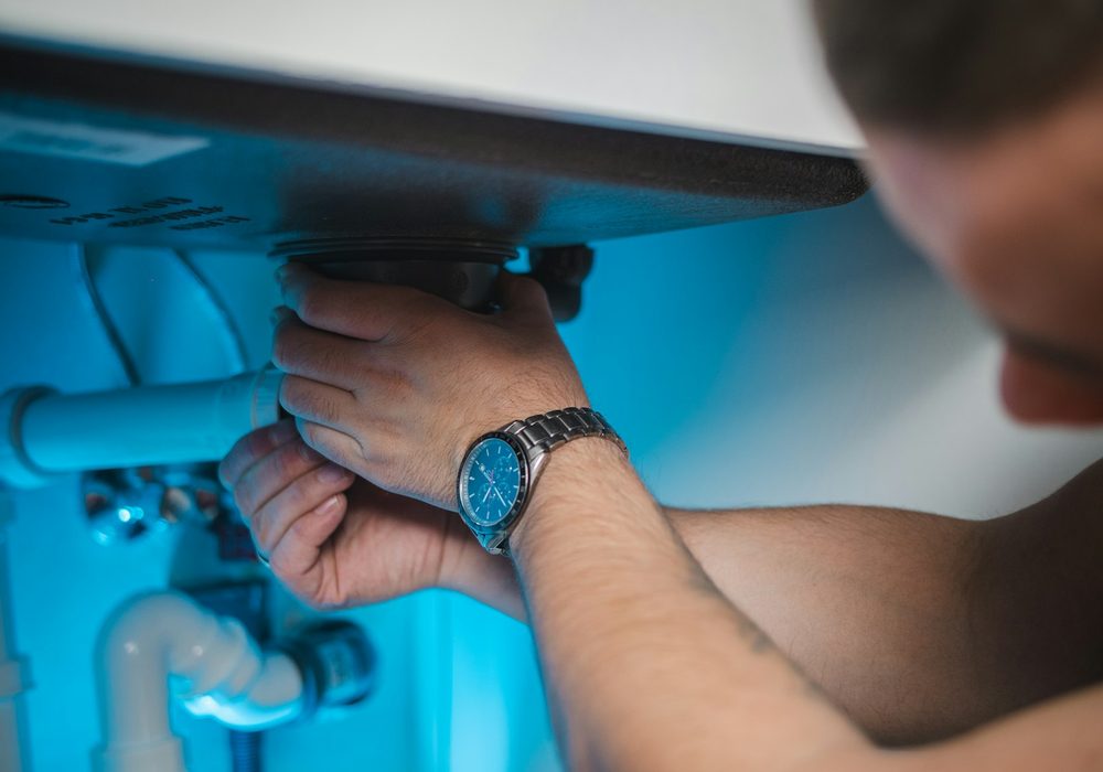Hands using a wrench on an under-sink pipe fitting